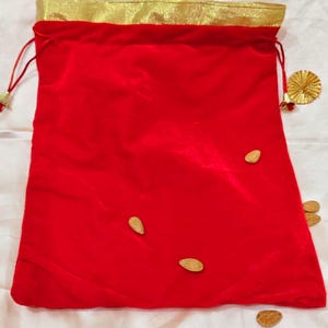 Puede incluir: Una bolsa roja de terciopelo con cordón y ribete dorado. La bolsa está decorada con varios objetos en forma de almendra. Varias piezas decorativas circulares doradas están dispersas.