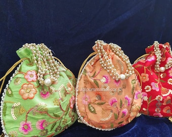 May include: Three embroidered drawstring pouches in shades of green, peach, and red. Each pouch features floral embroidery and is adorned with a beaded drawstring and a pearl accent. The pouches are displayed on a dark blue velvet surface.