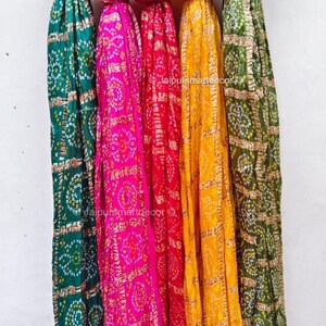 May include: Five vibrant scarves in shades of green, pink, red, yellow, and olive green, each featuring a repeating circular pattern. The scarves are displayed vertically, with the ends slightly frayed.
