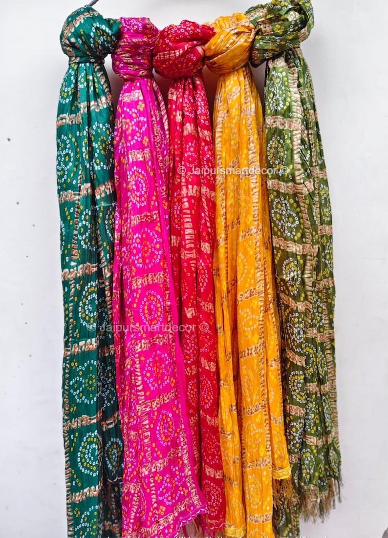 May include: Five vibrant scarves in shades of green, pink, red, yellow, and olive green, each featuring a repeating circular pattern. The scarves are displayed vertically, with the ends slightly frayed.