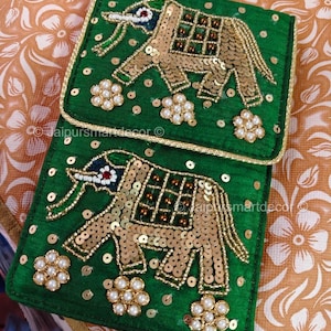 May include: Two green, rectangular, embroidered pouches with gold elephant designs. The elephants are embellished with gold sequins and beads. The pouches have a gold trim and are decorated with pearl-like flower clusters.