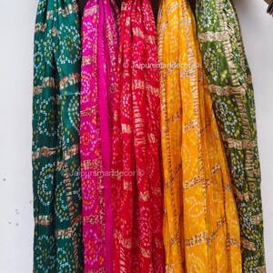 May include: A display of vibrant scarves in green, pink, red, yellow, and olive green. Each scarf has a repeating pattern of small circles and rectangular shapes. The scarves are hanging vertically, displaying their bright colours and designs.