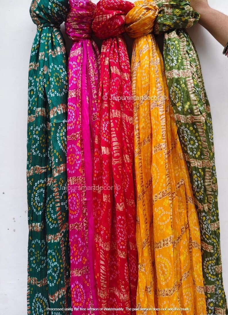 May include: A display of vibrant scarves in green, pink, red, yellow, and olive green. Each scarf has a repeating pattern of small circles and rectangular shapes. The scarves are hanging vertically, displaying their bright colours and designs.