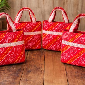May include: Four red tote bags with white handles and a white band across the middle. The bags have a repeating pattern of white and yellow dots on a red background. The bags are sitting on a wooden surface.