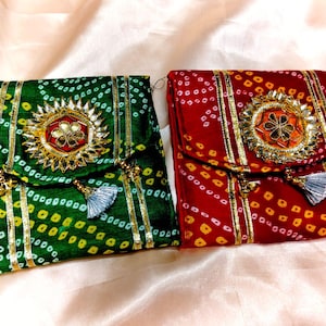 Puede incluir: Dos bolsas decorativas de tela. Una es verde con patrones de puntos amarillos y blancos, la otra es roja con patrones de puntos amarillos y blancos. Ambas tienen adornos dorados, un adorno circular central y una borla.