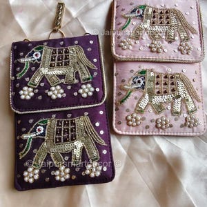 May include: Purple and pink embroidered elephant design phone pouches. The pouches feature a flap closure and a gold-colored chain. The elephant design is embellished with sequins and beads. The pouches are likely made of a satin-like material.