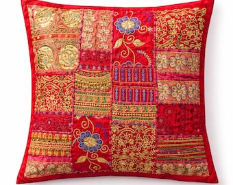 Puede incluir: Un cojín decorativo rojo cuadrado con un diseño de patchwork. El cojín presenta varios patrones bordados en oro, rosa y azul. El cojín tiene un borde rojo y probablemente está hecho de terciopelo o una tela similar.