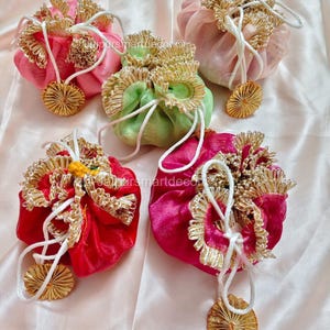 Può includere: Cinque sacchetti colorati con coulisse nei toni del rosa, rosso e verde. Ogni sacchetto è adornato con finiture color oro e un ciondolo circolare abbinato. I sacchetti sono legati con cordoncini bianchi.