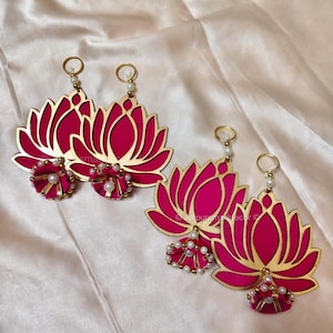 May include: Hot pink lotus flower earrings with gold trim and pearl accents. The earrings have a floral design and a small cluster of pearls and gold beads at the base. The earrings are hanging from a gold hoop.