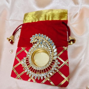 Può includere: Pochette in velluto rosso con finiture dorate e un abbellimento decorativo dorato e specchiato. La pochette ha una chiusura con coulisse con nappe dorate. La parte anteriore della pochette presenta un motivo a rombi dorati.