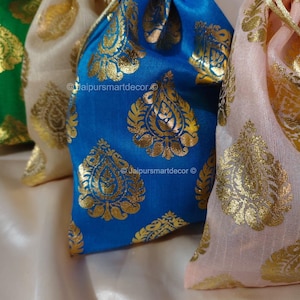 May include: Close-up of several drawstring bags in various colors, including blue, cream, green, and pink. Each bag features a gold paisley pattern. The bags are made of a silky fabric and are gathered at the top.