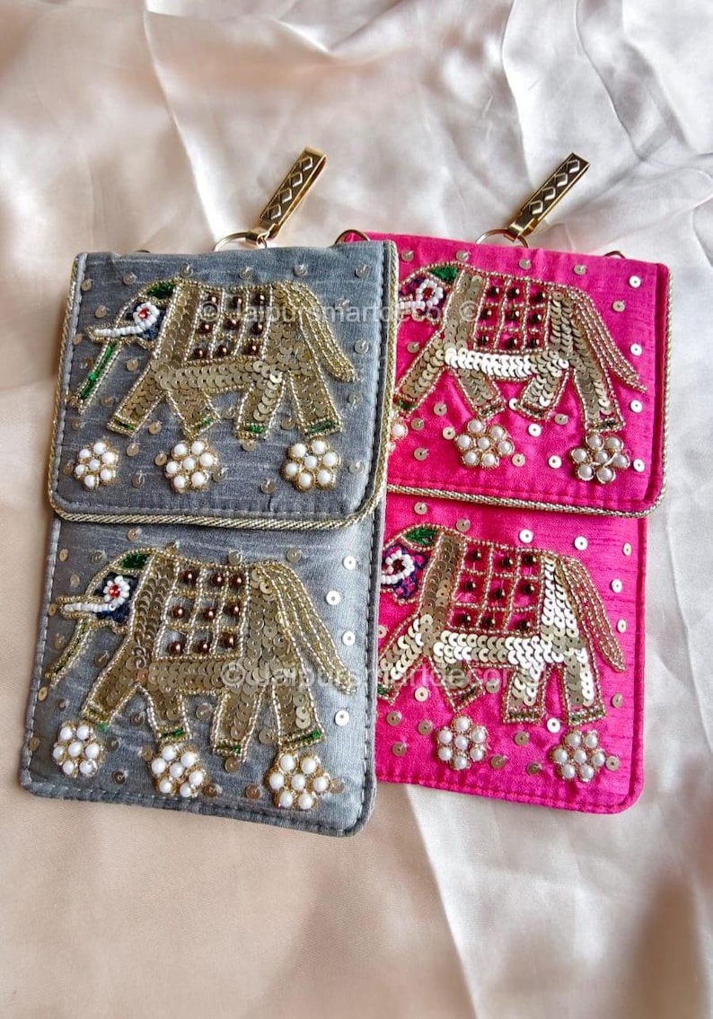 May include: Two embellished phone pouches, one gray and one pink, with gold elephant designs. The elephants are adorned with sequins and beads. Each pouch has a gold-tone clasp and a small floral embellishment.