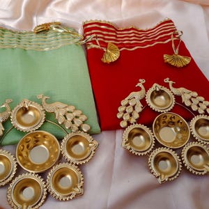 May include: Two decorative pouches, one green and one red, with gold trim and tassels. Each pouch is adorned with a peacock design and several small, gold-colored bowls, likely for decorative purposes.