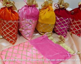 May include: A collection of colorful velvet pouches in orange, pink, yellow, and red, with gold diamond-patterned accents. Each pouch has a drawstring closure and gold trim. The pouches are arranged on a light-colored fabric.