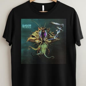May include: Black t-shirt with the album art for "The Mollusk" by Ween. The artwork shows a surreal aquatic creature with multiple eyes, tentacles, and a purple centre, against a dark teal background. The band name and album title are printed in teal.