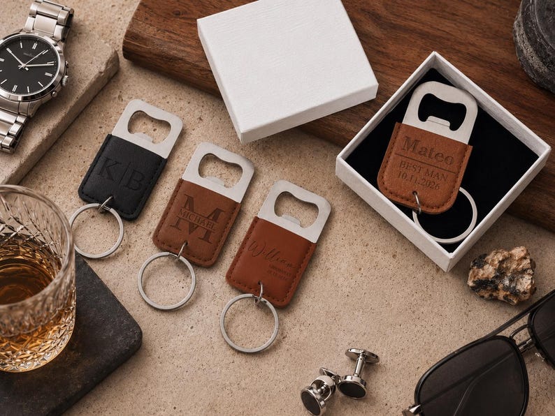May include: Four rectangular bottle opener keychains with leather-like covers in black and brown. Three are laid out with engraved initials or names, while one is inside a white gift box with the text Mateo, BEST MAN, and 10.11.2026 engraved.