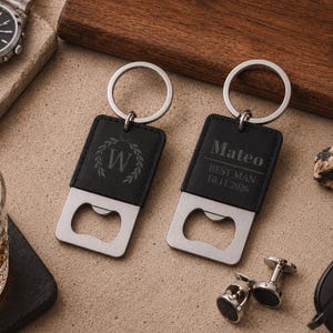 May include: Two rectangular black leather keychains with integrated silver-tone metal bottle openers. One keychain features a laurel wreath design with the letter W, while the other is engraved with the text Mateo, BEST MAN, and 10.11.2026.