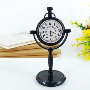 May include: A black, vintage-style desk clock with a white clock face and black numerals. The clock has a round face and is supported by a black stand. The clock's face displays the numbers 1 through 24.