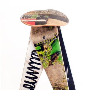 May include: A stool made from repurposed skateboards. The seat is a single skateboard with a red, white, and black design. The legs are made from two skateboards with a green and black design. The legs are connected by a black spring.