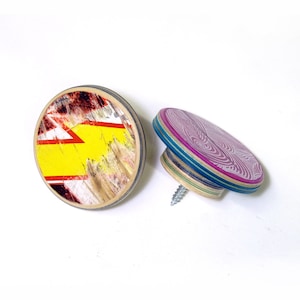 May include: Two round wooden knobs with colorful patterns. One knob has a yellow, red, and black abstract design. The other knob has a purple and white swirl pattern.