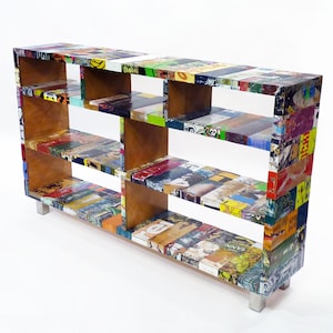 Puede incluir: Una estantería rectangular multicolor con múltiples estantes. El exterior está cubierto con un collage de imágenes coloridas, mientras que los estantes interiores son de un tono de madera natural. La estantería tiene cuatro patas plateadas.