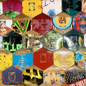 Puede incluir: Una pared cubierta con azulejos hexagonales hechos de tablas de skate recicladas. Los azulejos están pintados en varios colores y patrones, incluyendo rojo, azul, verde, amarillo y negro. Algunos azulejos tienen texto en ellos, como "WILD" y "FANTA", mientras que otros tienen diseños gráficos.