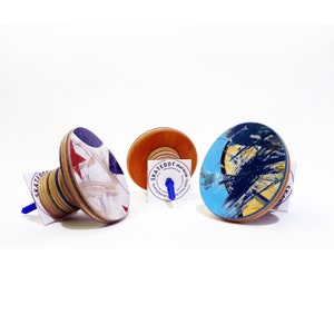 Op de afbeelding: Drie wandhaken gemaakt van gerecyclede skateboards. Elke haak heeft een ander ontwerp met een blauw, rood en wit kleurenschema. De haken zijn bevestigd aan een witte muur.