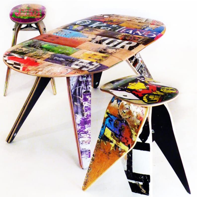 May include: A set of colourful furniture made from recycled skateboards. The table is oval shaped and has a unique design. The stools have three legs and are also made from recycled skateboards.