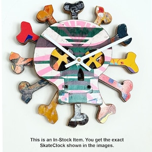 May include: A colorful skull-shaped wall clock with crossbones. The clock face features a vibrant mix of pink, green, yellow, and blue hues. White clock hands indicate the time. The text "This is an In-Stock Item. You get the exact SkateClock shown in the images."