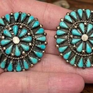 May include: A pair of circular silver earrings featuring a cluster design with multiple teardrop-shaped turquoise stones arranged in concentric patterns around a central silver dot, accented by twisted silver wire detailing.