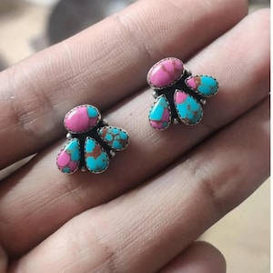 Pode incluir: Um par de brincos de pressão com um design de aglomerado. Cada brinco tem uma pedra rosa oval central rodeada por quatro pedras turquesas em forma de gota. As pedras são fixadas em uma moldura de metal prateado.