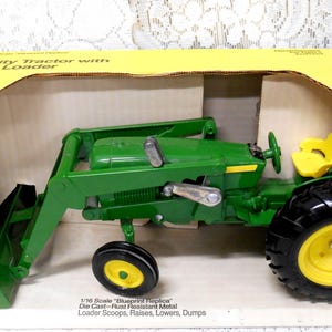 May include: A green and yellow toy utility tractor with an end loader, displayed in its original box. The tractor has black tires with yellow rims and a yellow seat. The box is yellow and green and reads "Utility Tractor with End Loader."
