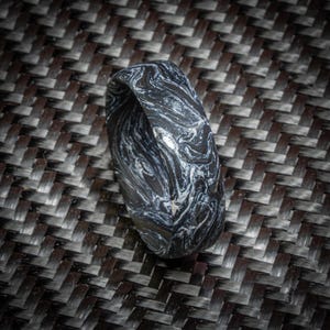 May include: A black and white marbled ring. The ring has a swirling pattern of white against a black background. The ring is made of a solid material and has a smooth, polished finish. The ring is a band style.