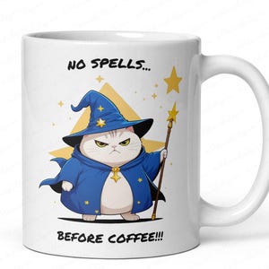 Op de afbeelding: Witte keramische mok met een cartoonkat verkleed als tovenaar, met een blauwe mantel en hoed, en een staf met een ster. De tekst "NO SPELLS... BEFORE COFFEE!!!" staat in het zwart.
