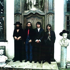 May include: Four men stand in front of a large wooden door. They are dressed in dark suits and coats, with one wearing a hat. A stone bust is on the right. The image has a vintage, classic aesthetic.