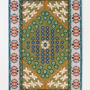 May include: A rectangular rug with a green central field, featuring white floral and blue and yellow geometric patterns. The rug has a pink and teal border with repeating floral designs. The rug is approximately 36 inches by 60 inches.