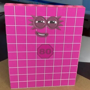 May include: A bright pink block with a grid pattern and a cartoon face. The block features a smiling face with sleepy eyes and the number 80 in a red octagon. This educational toy is designed for learning.