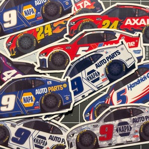Puede incluir: Una colección de pegatinas troqueladas con varios coches de carreras NASCAR. Las pegatinas muestran diferentes diseños de coches, incluyendo los números 9, 24 y 5, con logotipos de patrocinadores como NAPA, Axalta y HendrickCars.com. Los coches son de varios colores, incluyendo azul, rojo y blanco.