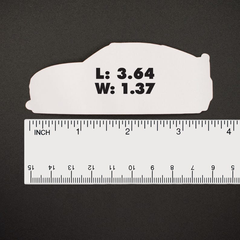 May include: A white car-shaped sticker with the text "L: 3.64 W: 1.37" printed on it. The sticker is measured with a ruler in inches. The car shape is a side profile of a coupe.