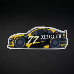 May include: A sticker depicting a black and yellow race car with the number 77 and the name "ZEIGLER". The wheels display "GOOD YEAR" and "EAGLE" branding. The car is set against a black background.