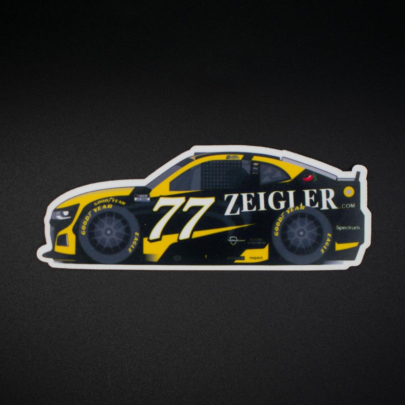 May include: A sticker depicting a black and yellow race car with the number 77 and the name "ZEIGLER". The wheels display "GOOD YEAR" and "EAGLE" branding. The car is set against a black background.