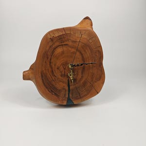 May include: A unique wooden clock crafted from a cross-section of a tree trunk. The clock face displays natural wood grain patterns in shades of brown and tan. The clock hands and mechanism are made of brass. A decorative and functional home decor item.