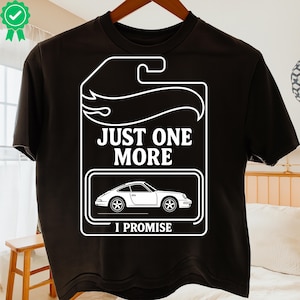 Könnte beinhalten: Schwarzes T-Shirt mit weißem Grafikdesign. Das Design zeigt den Text "JUST ONE MORE I PROMISE" über einer weißen Autoillustration in einem rechteckigen Rahmen, der einer Spielzeugauto-Verpackung ähnelt.