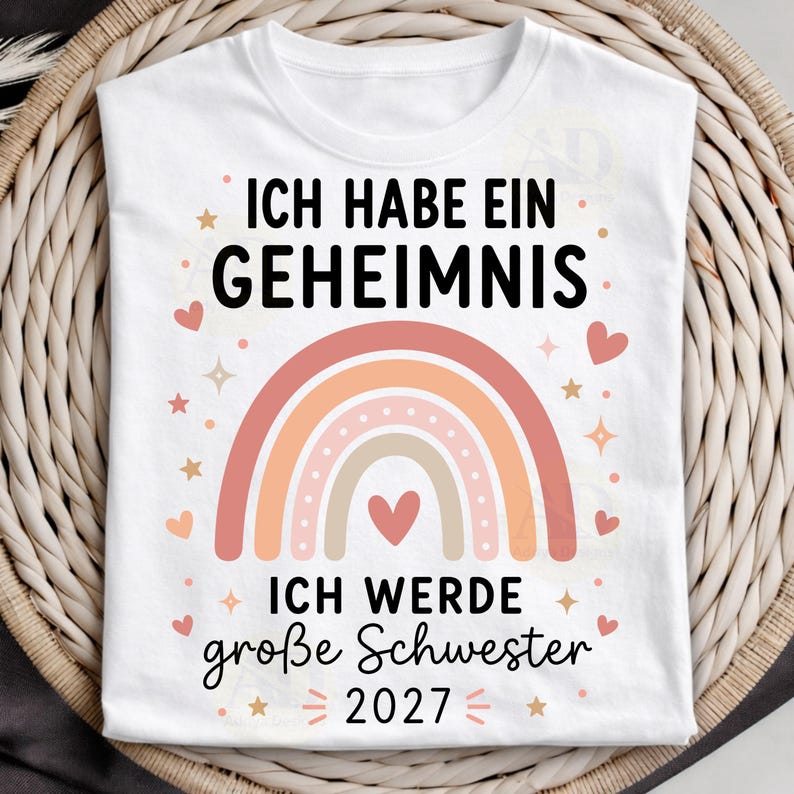 May include: A white t-shirt featuring a graphic with the text ICH HABE EIN GEHEIMNIS and ICH WERDE gro&szlig;e Schwester 2027 in black lettering. The design includes a multi-colored pastel rainbow, small pink hearts, and star shapes surrounding the text.