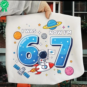 May include: White fabric featuring a space-themed design with the text "I WAS 6 NOW I'M 7" in blue. The design includes planets, stars, and an astronaut on a rocket. A fun birthday theme.