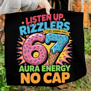 May include: Black tote bag with a colorful graphic design. The design features the words "LISTEN UP RIZZLERS" and "AURA ENERGY NO CAP". The number "67" is designed as a donut and ice cream cone.