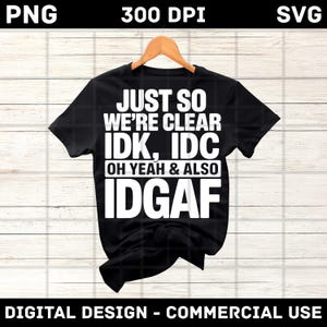Puede incluir: Camiseta negra con el texto blanco "JUST SO WE'RE CLEAR IDK, IDC OH YEAH & ALSO IDGAF". La camiseta está colgada en una percha de madera. El fondo es de madera clara. Diseño digital para uso comercial.