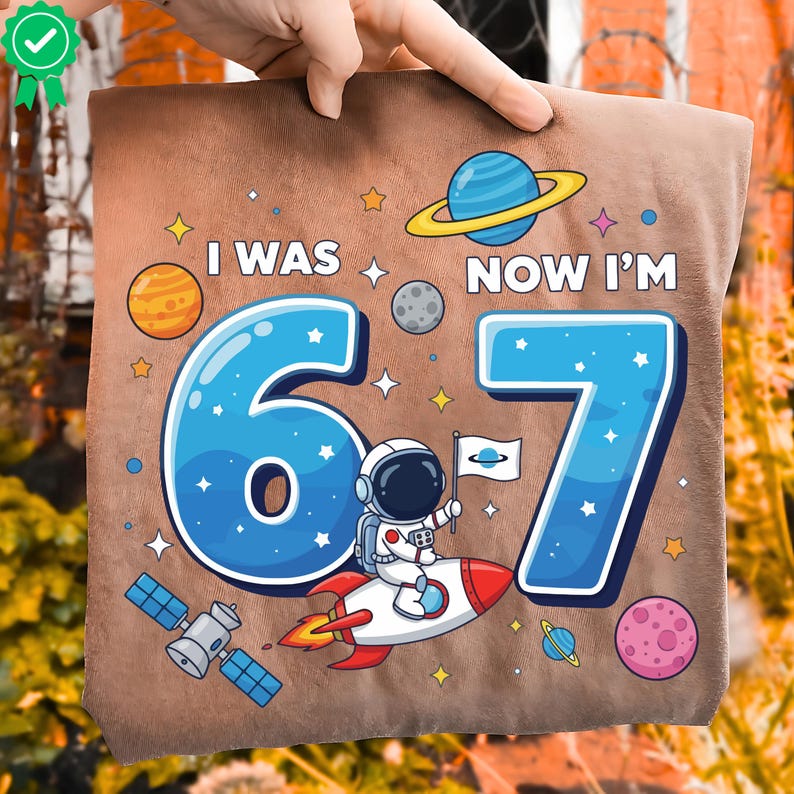 May include: A brown cushion with a space theme, featuring the text "I WAS 6, NOW I'M 7". The design includes planets, stars, a satellite, and an astronaut on a rocket. The numbers 6 and 7 are in blue with white outlines.