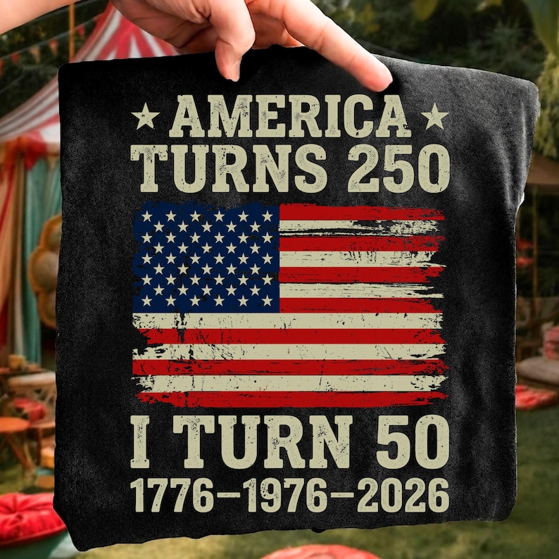 Puede incluir: Camiseta negra con el texto "AMERICA TURNS 250" y "I TURN 50". El dise&ntilde;o incluye una bandera estadounidense desgastada en rojo, blanco y azul. Las fechas 1776-1976-2026 est&aacute;n impresas debajo.