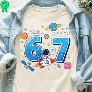 May include: Cream-coloured t-shirt with a space-themed graphic. The design features the text "I WAS 6, NOW I'M 7" in blue, along with planets, stars, and an astronaut on a rocket. A fun birthday shirt.